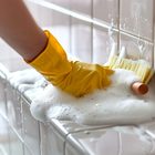 Gloved hand scrubbing bathroom tile with foaming cleaner